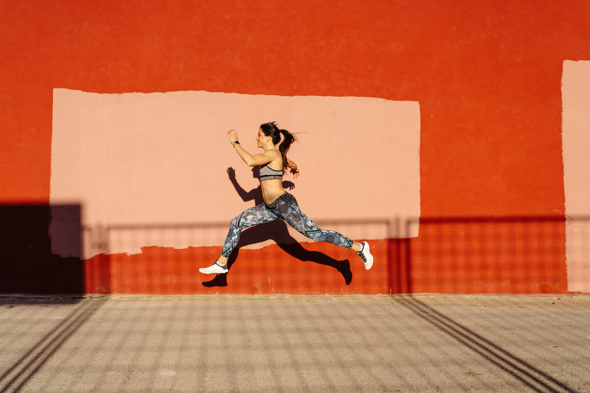 Slim sportswoman leaping against weathered wall